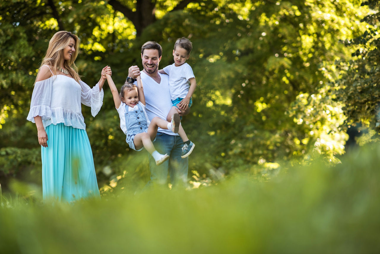 Junge glückliche Eltern schaukeln ihr kleines Mädchen im Park, während der Vater den kleinen Jungen hält.