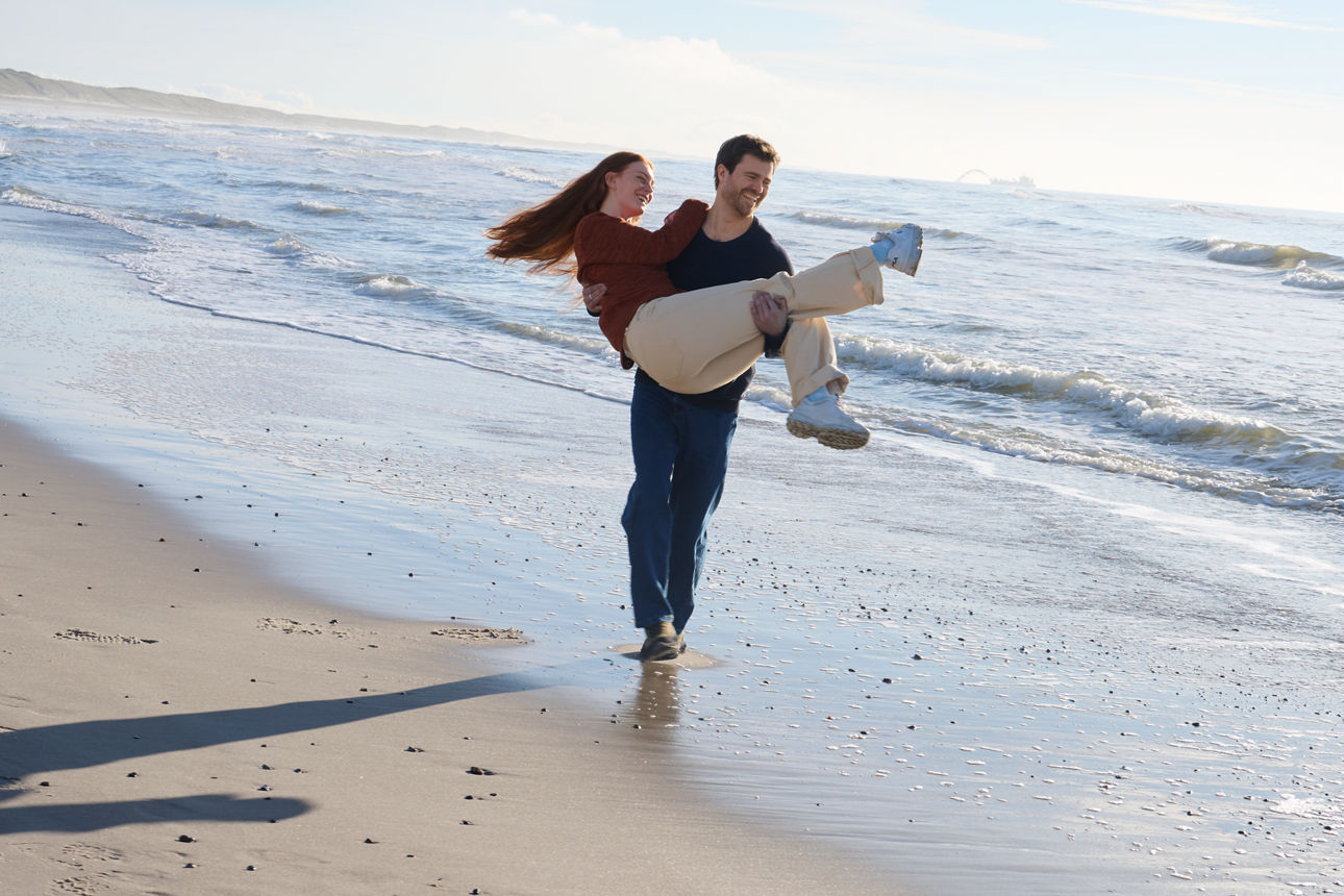 Mann trägt Frau auf dem Arm am Strand spazieren