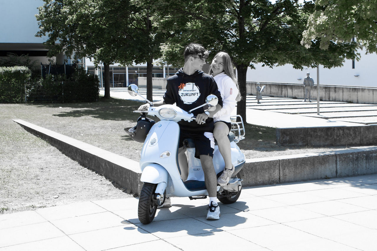 Zwei lachende junge Menschen auf einem Roller