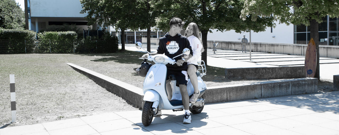 Junge und Mädchen sitzen auf einem Roller.
