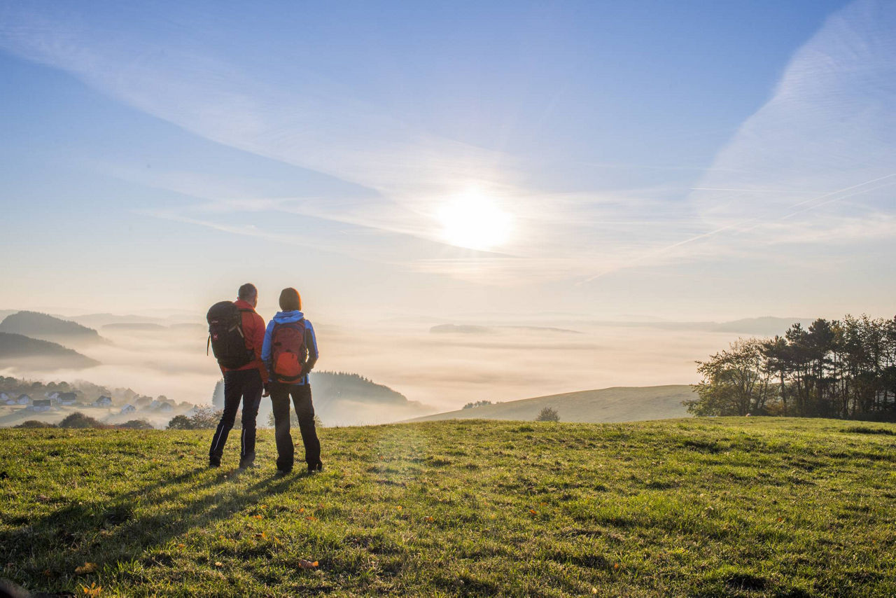 Zwei Wanderer blicken auf eine Mittelgebirgslandschaft.