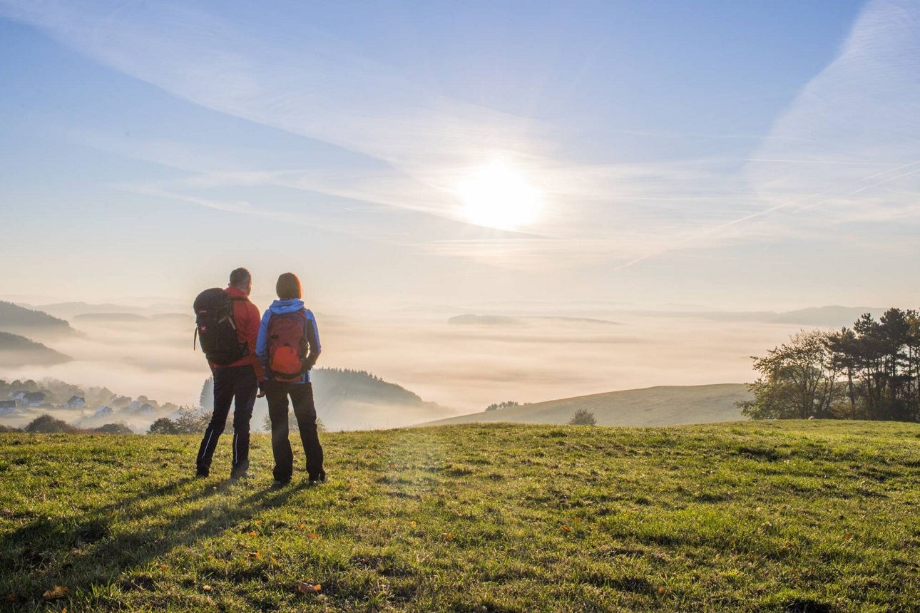 Zwei Wanderer blicken auf eine Mittelgebirgslandschaft.