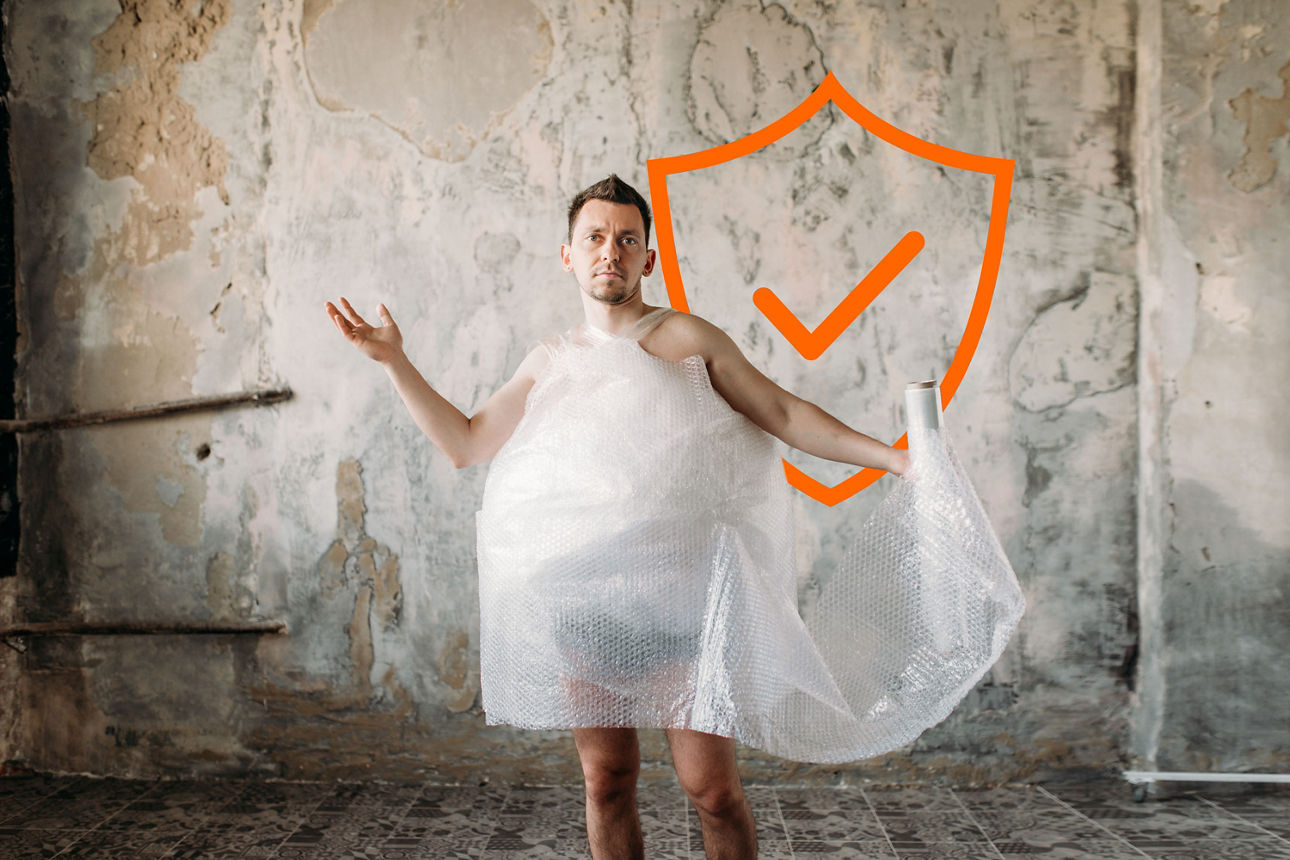 Person steht barfuß in einem Raum, trägt Luftpolsterfolie um den Körper und hält eine Rolle Luftpolsterfolie. Im Hintergrund ist ein orangefarbenes Schild mit Häkchen zu sehen.