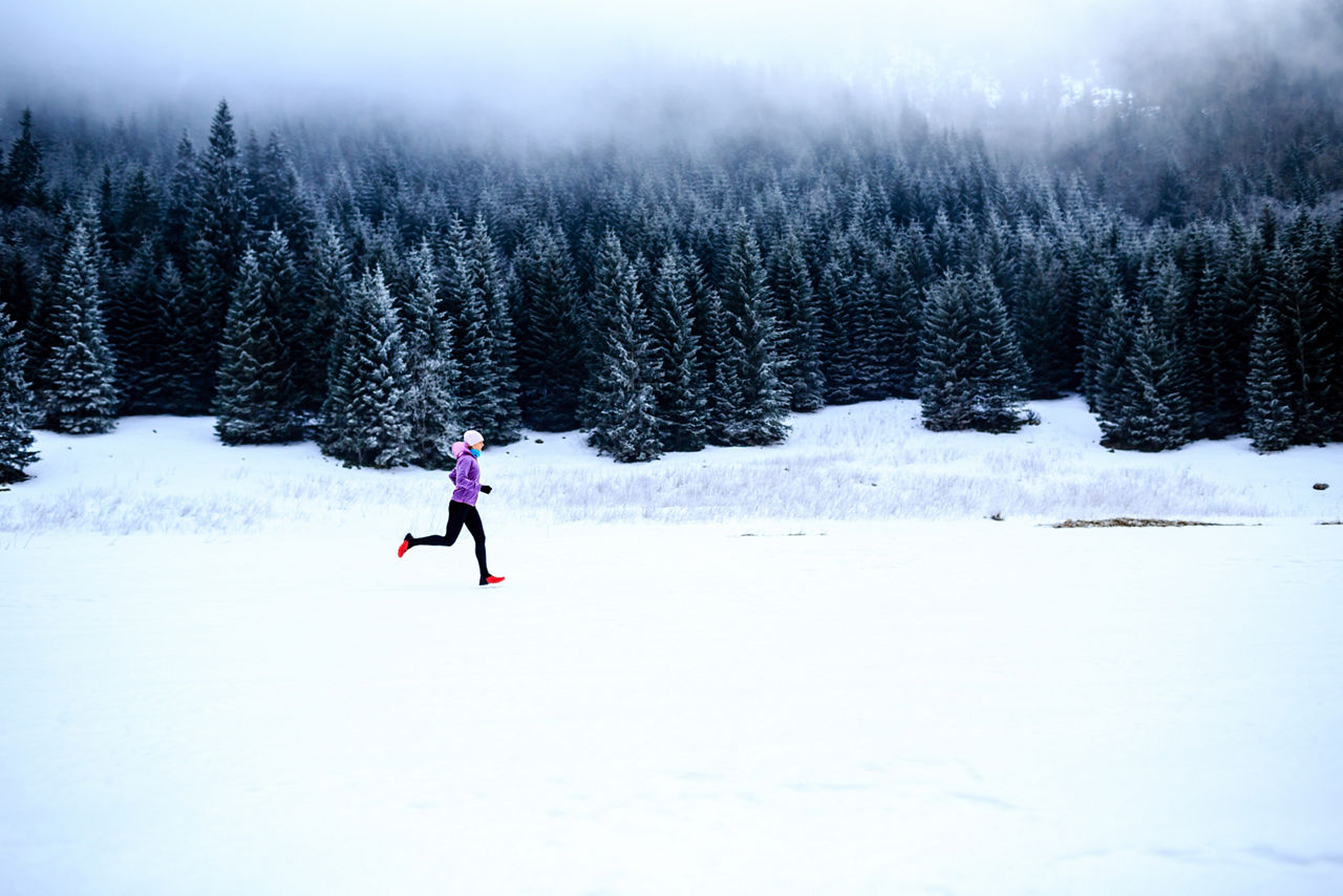 Sport, fitness inspiration and motivation. Young happy woman cross country running in mountains on snow, winter day. Female trail runner jogging exercising outdoors.