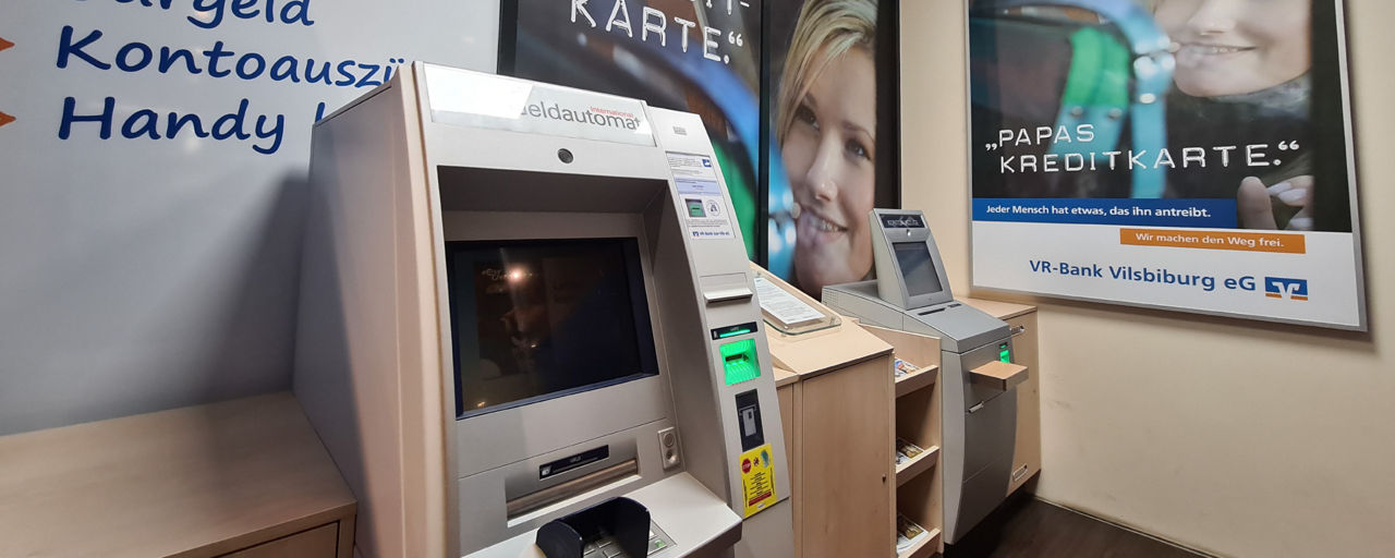 Zwei SB-Geräte nebeneinander. Im Hintergrund sind Plakate über Kreditkarten aufgehängt.