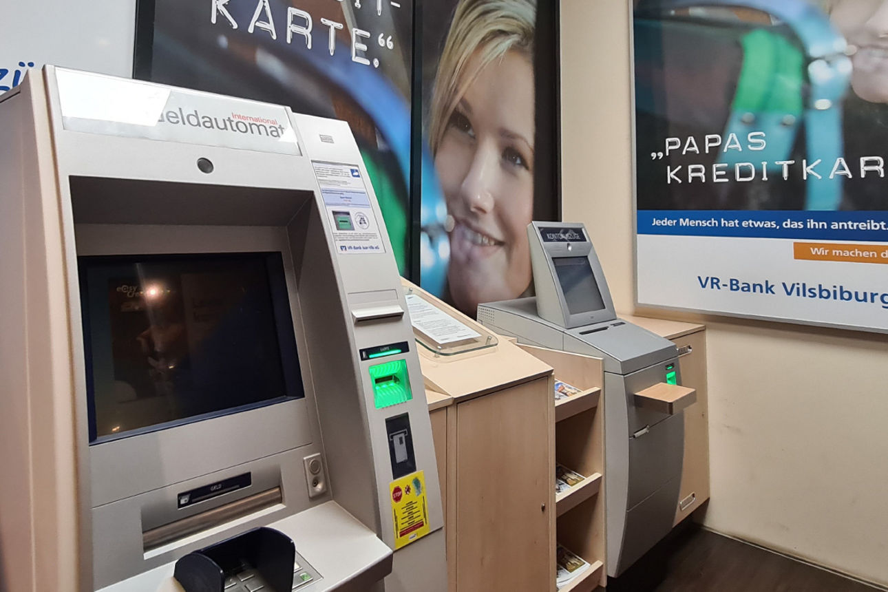 Zwei SB-Geräte nebeneinander. Im Hintergrund sind Plakate über Kreditkarten aufgehängt.