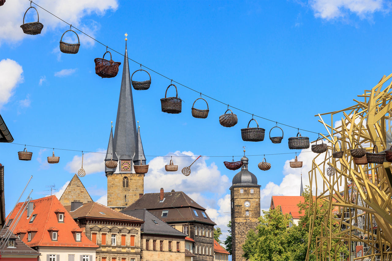 Blick auf die Stadtpfarrkirche Mariä Himmelfahrt mit Gebäuden und hängenden Körben im Vordergrund