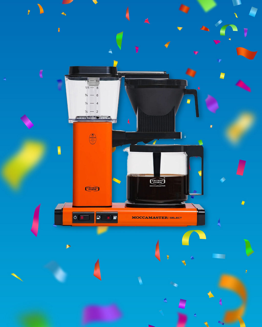 Eine orange-farbene Kaffeemaschine "Moccamaster" vor einem blauen Hintergrund mit Konfetti