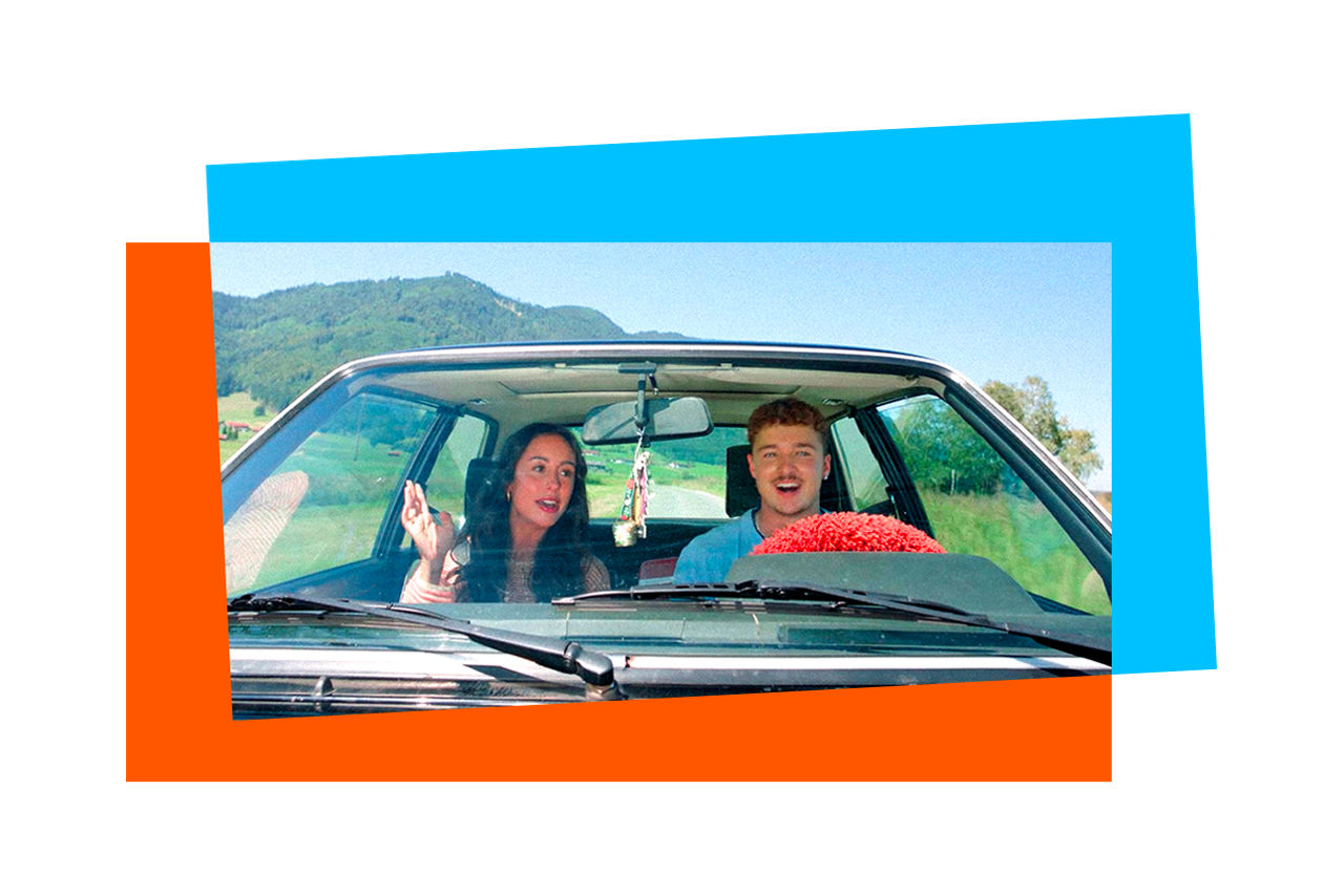 Eine Frau und ein Mann fahren im Auto und durch eine Berglandschaft.
