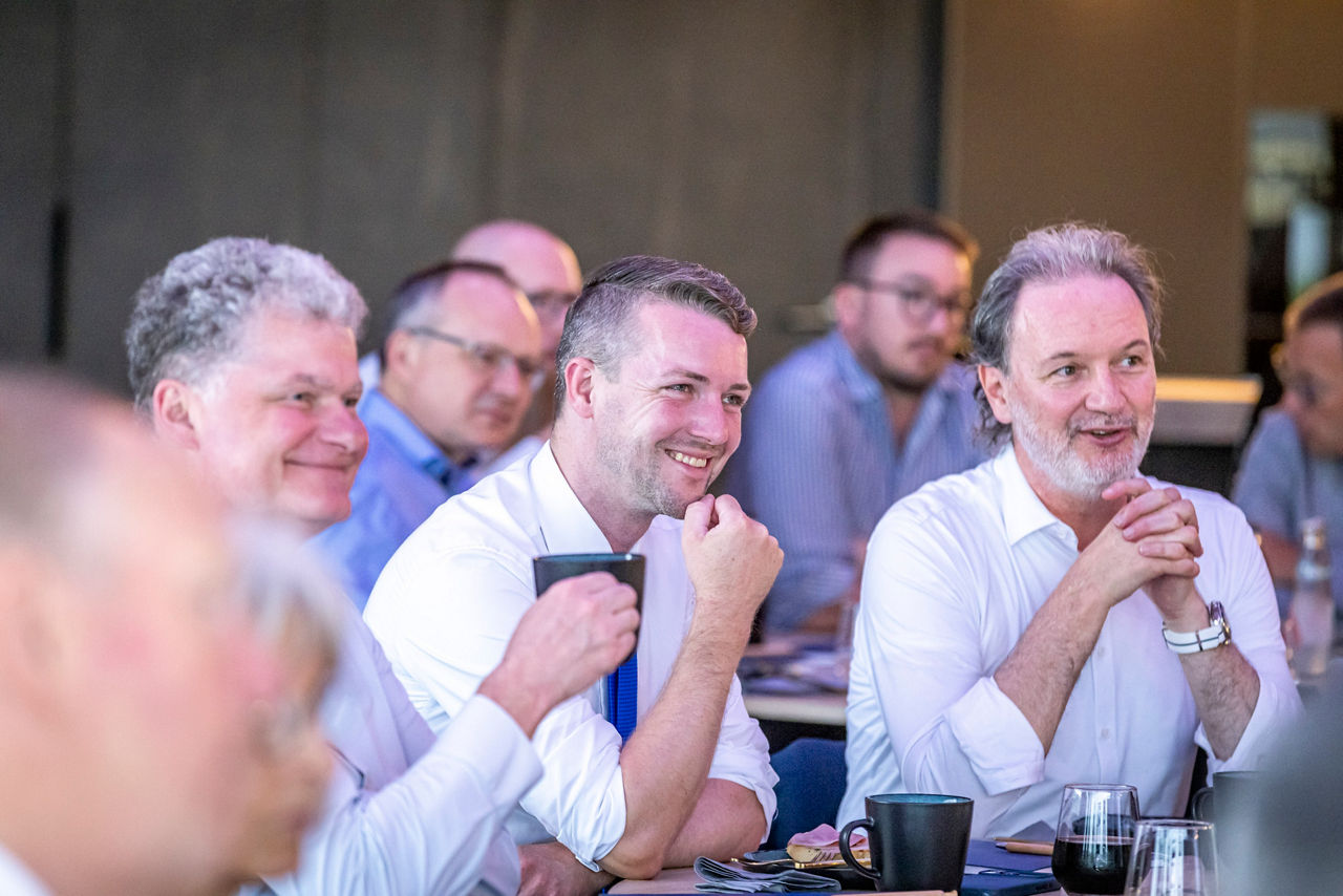 Während des Vortrags: Herren in Businesskleidung am Tisch, lachend