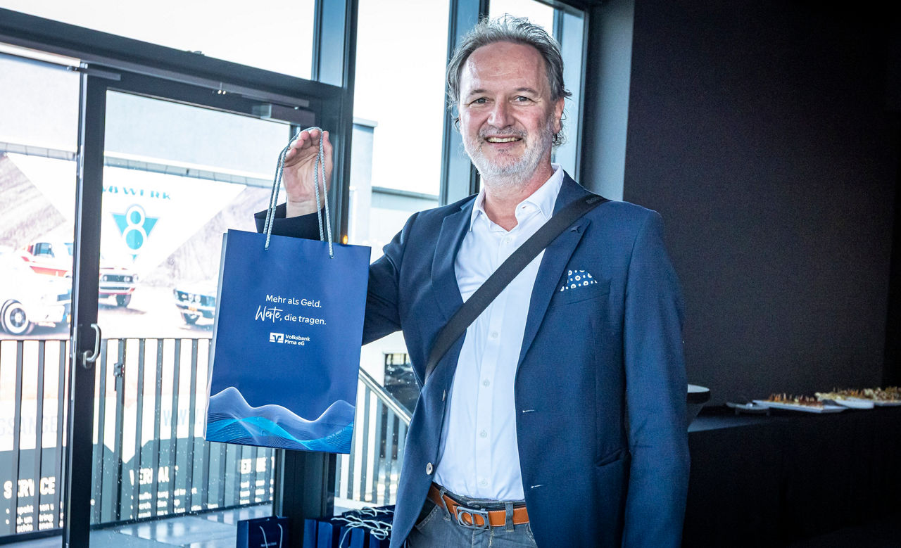 Mann im Anzug präsentiert Volksbank-Geschenktüte und freut sich