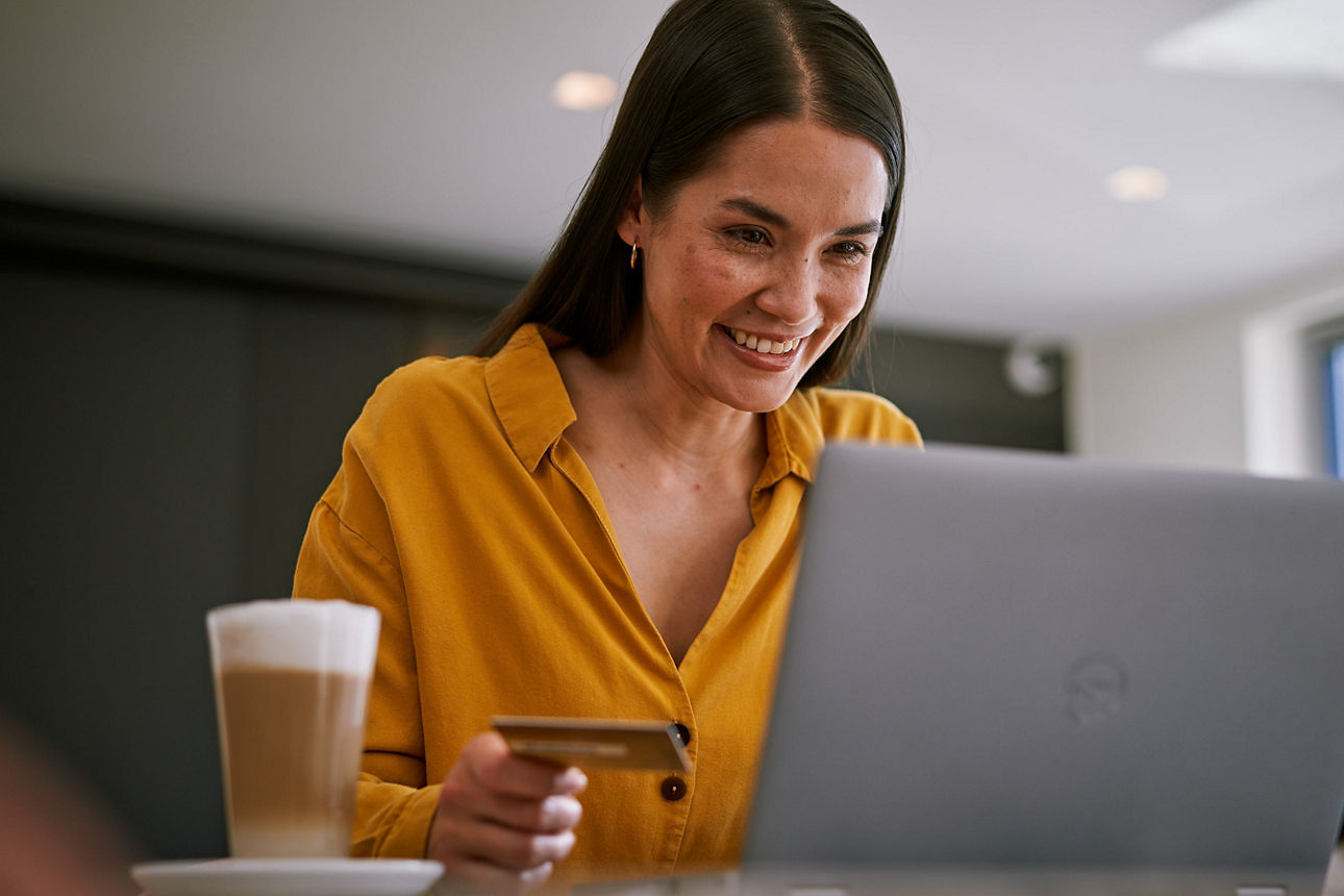 Junge Frau mit Laptop in einem Cafe mit ihrer girocard in der Hand