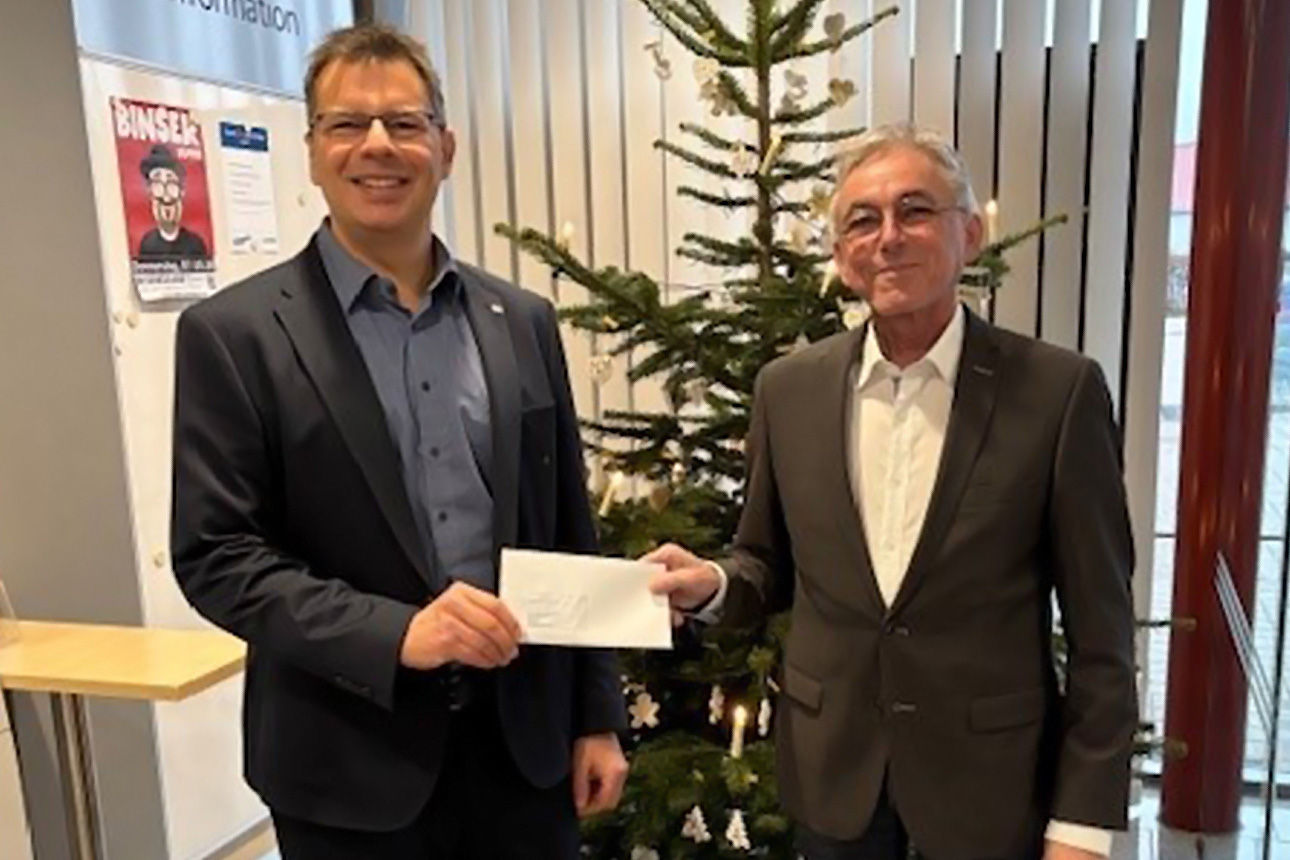 Zwei Männer lächeln in die Kamera. Sie halten einen Briefumschlag in der Hand.