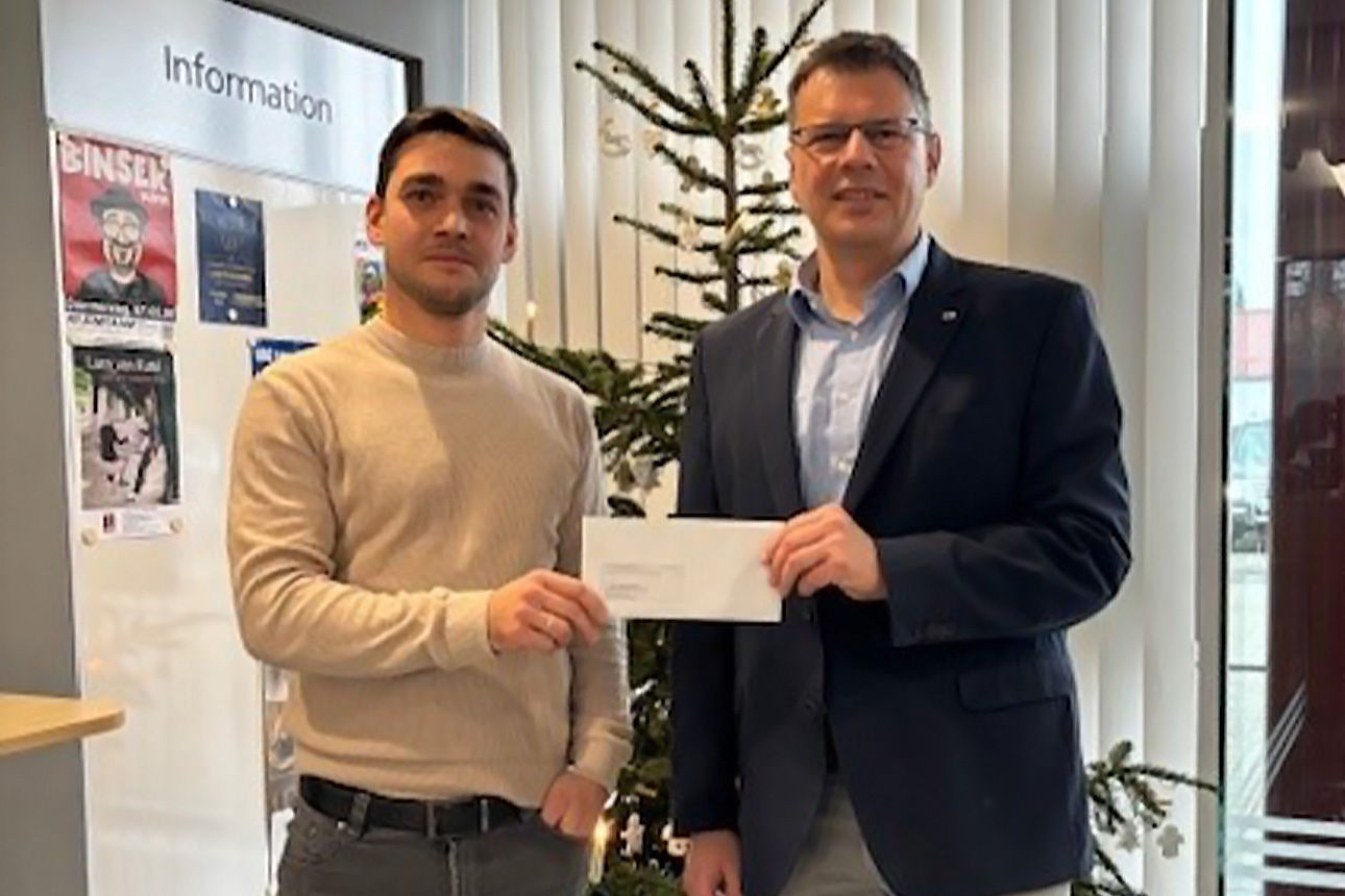 Zwei Männer lächeln in die Kamera. Sie halten einen Briefumschlag in der Hand.