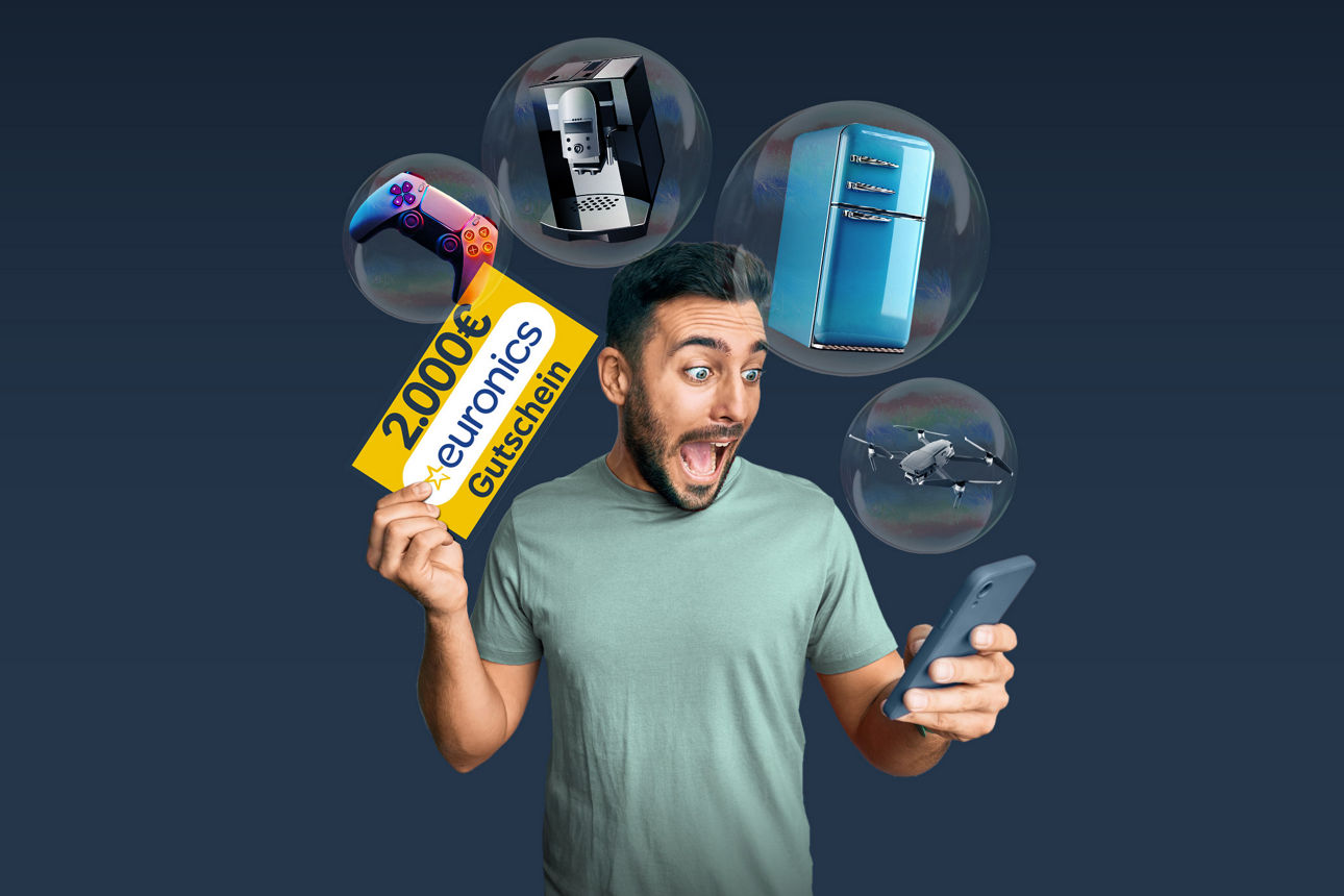 Mann schaut euphorisch auf ein Smartphone und einem 2.000 € euronics Gutschein in der Hand. 