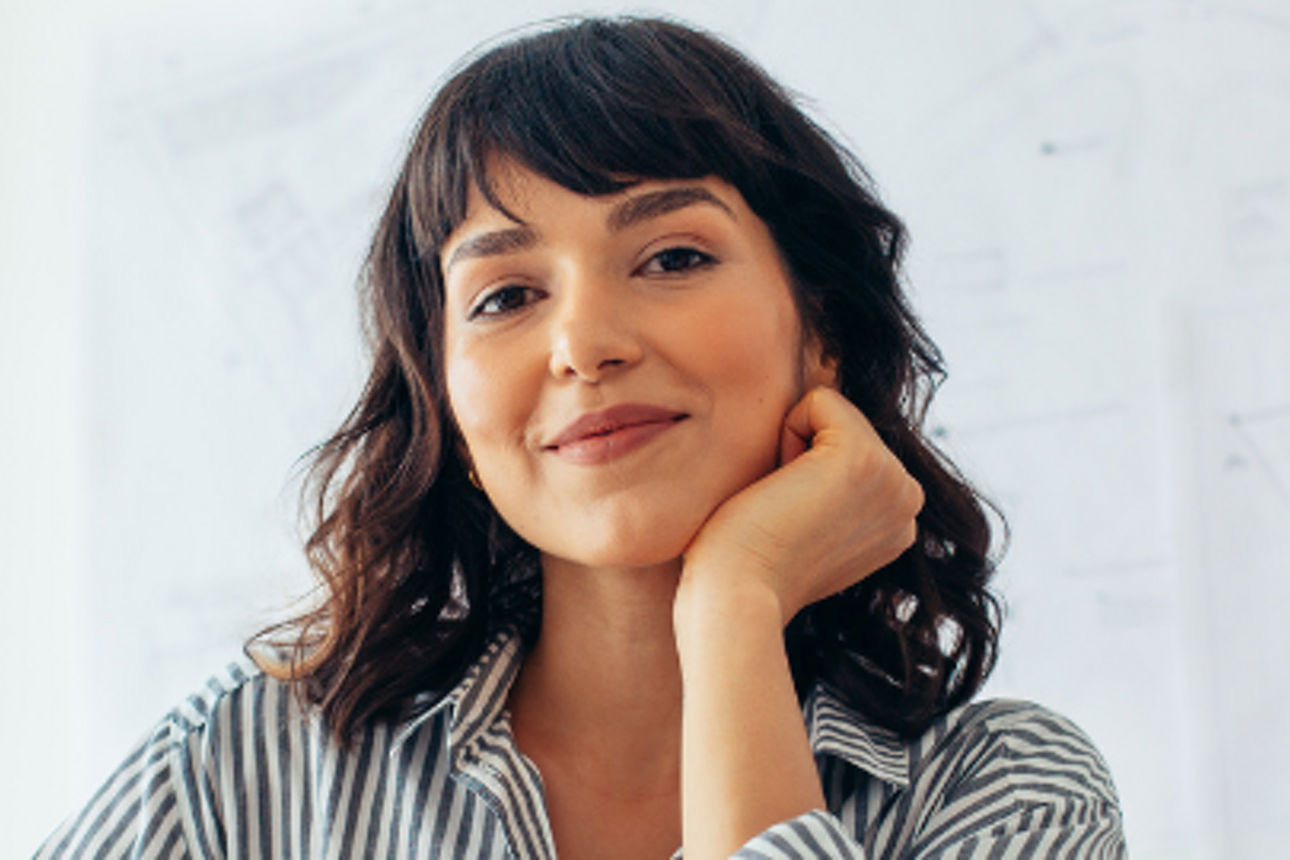 Frau mit gestreifter Bluse sitzt vor einem Laptop und lächelt