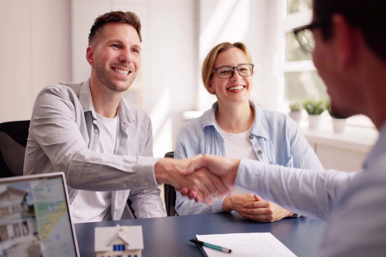 Berater und Paar besprechen sich zum Thema Immobilien und begrüßen sich mit Handschlag.