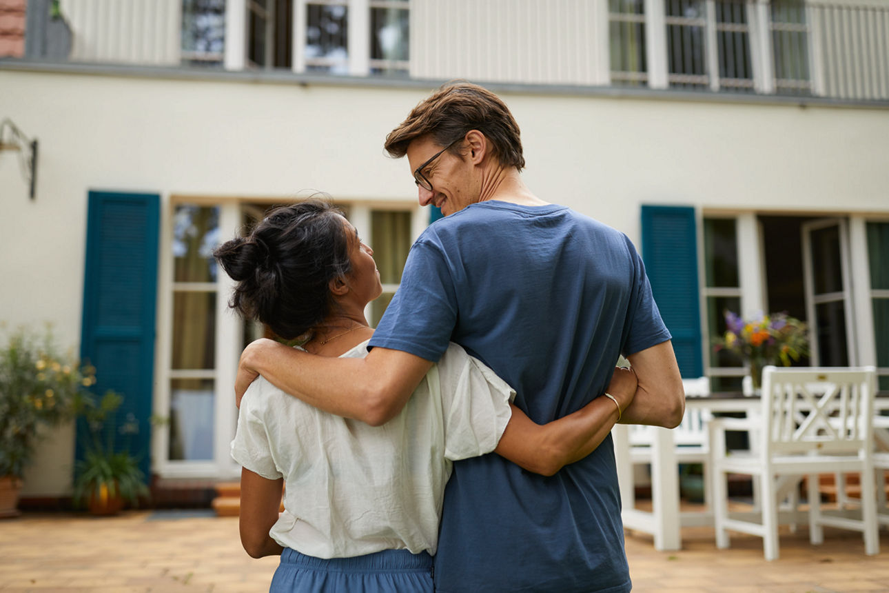 Mann und Frau laufen in einer Umarmung auf ein Haus zu. 