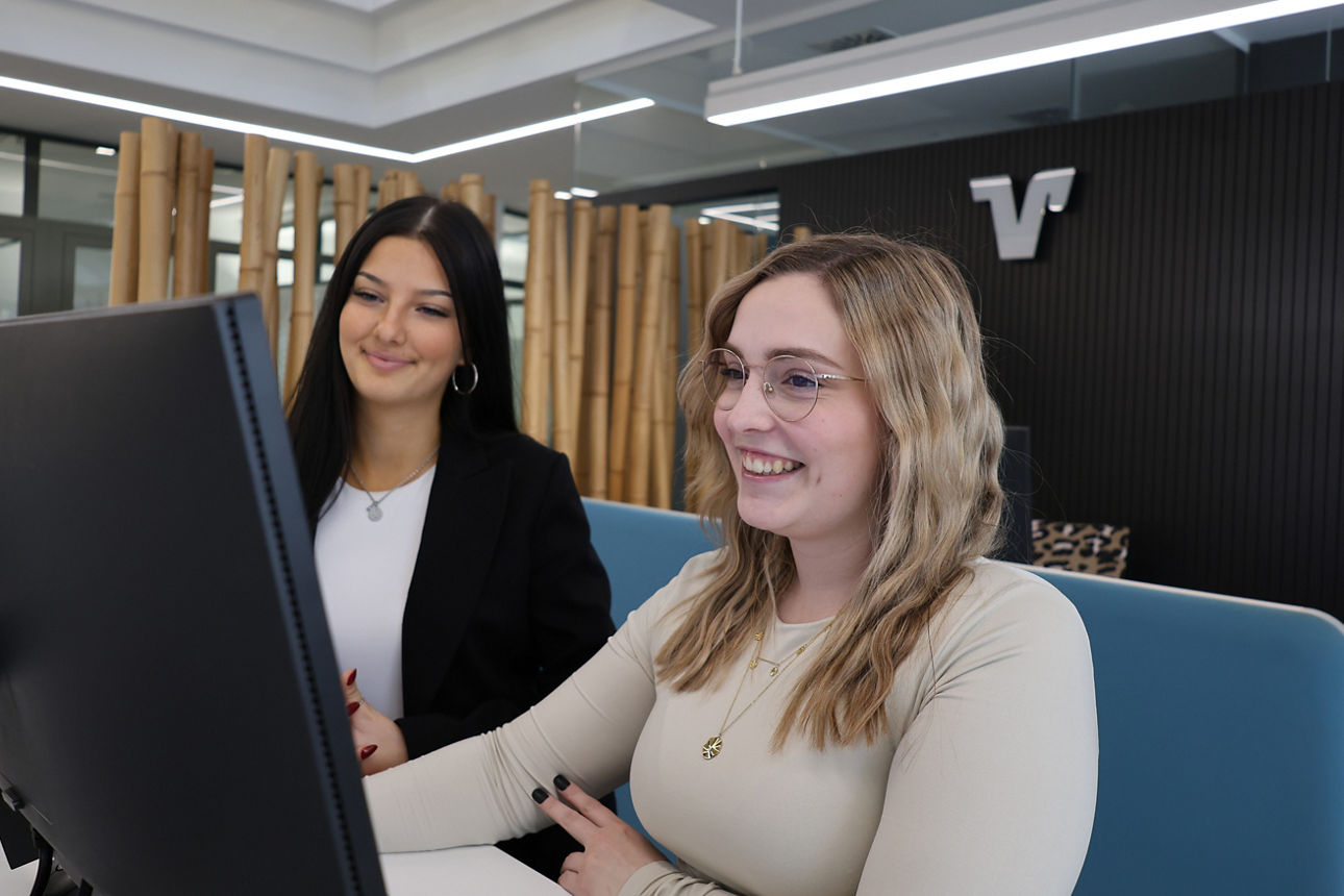 Eine Frau mit Headset sitzt lächelnd an ihrem Arbeitsplatz