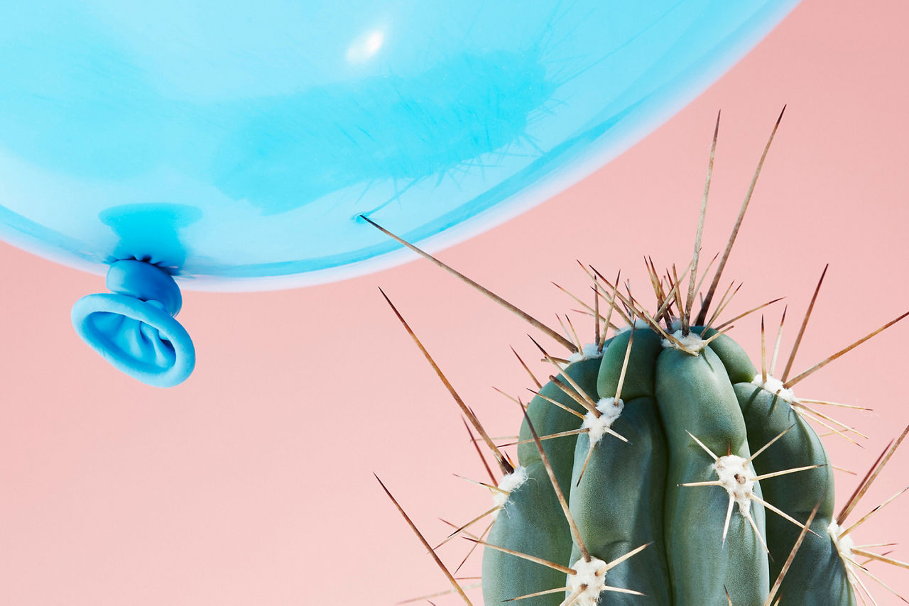 Ein blauer Luftballon wird von einem Kaktus angepikst