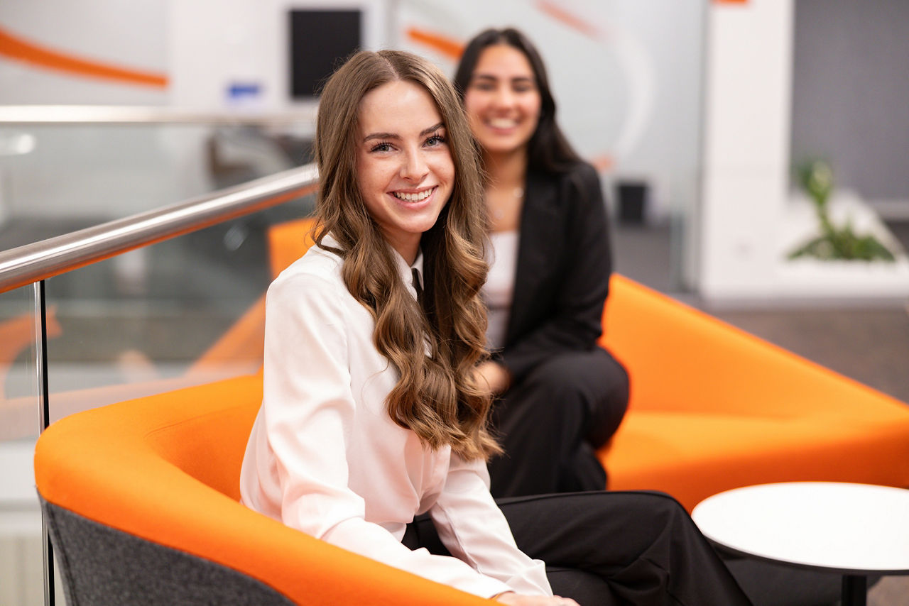 Zwei junge Frauen sitzen auf einem orangenen Sofa und lächeln in die Kamera