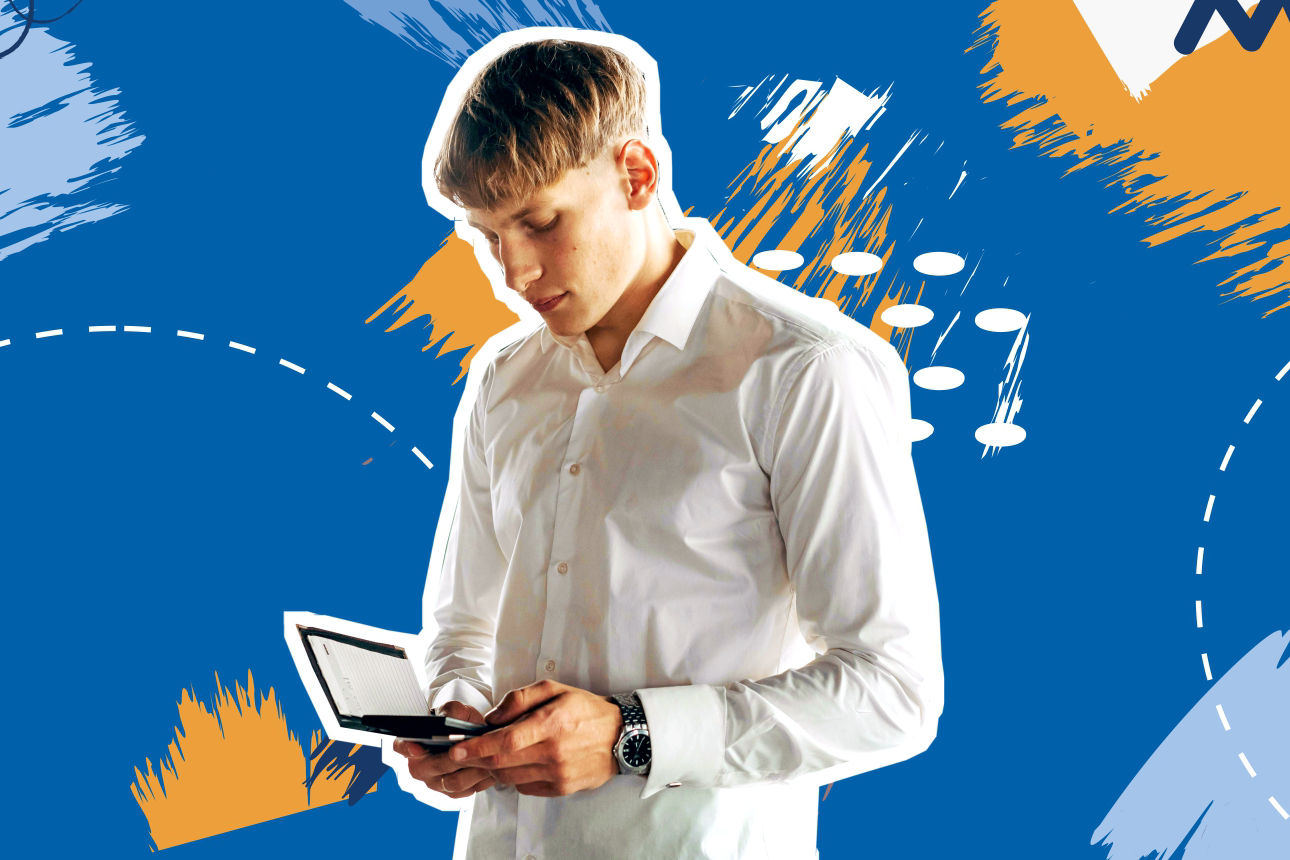 Junger Mann steht vor einem blauen Hintergrund und schaut in sein Notizbuch.