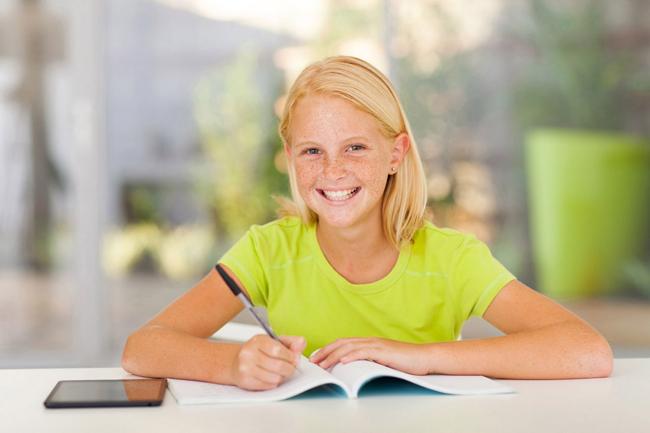 Schülerin macht Hausaufgaben und lächelt in die Kamera