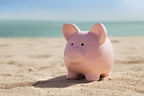 Ein rosa Sparschwein im Sand am Meer.