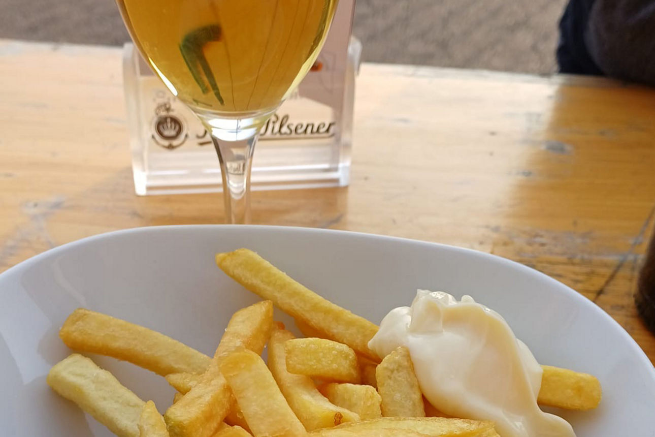 Ein Teller mit Pommes, Currywurst und Mayo - dahinter steht ein Bierglas