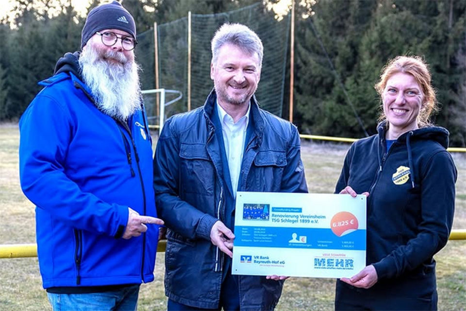 Zwei Männer und eine Frau halten die Crowdfunding-Tafel in den Händen