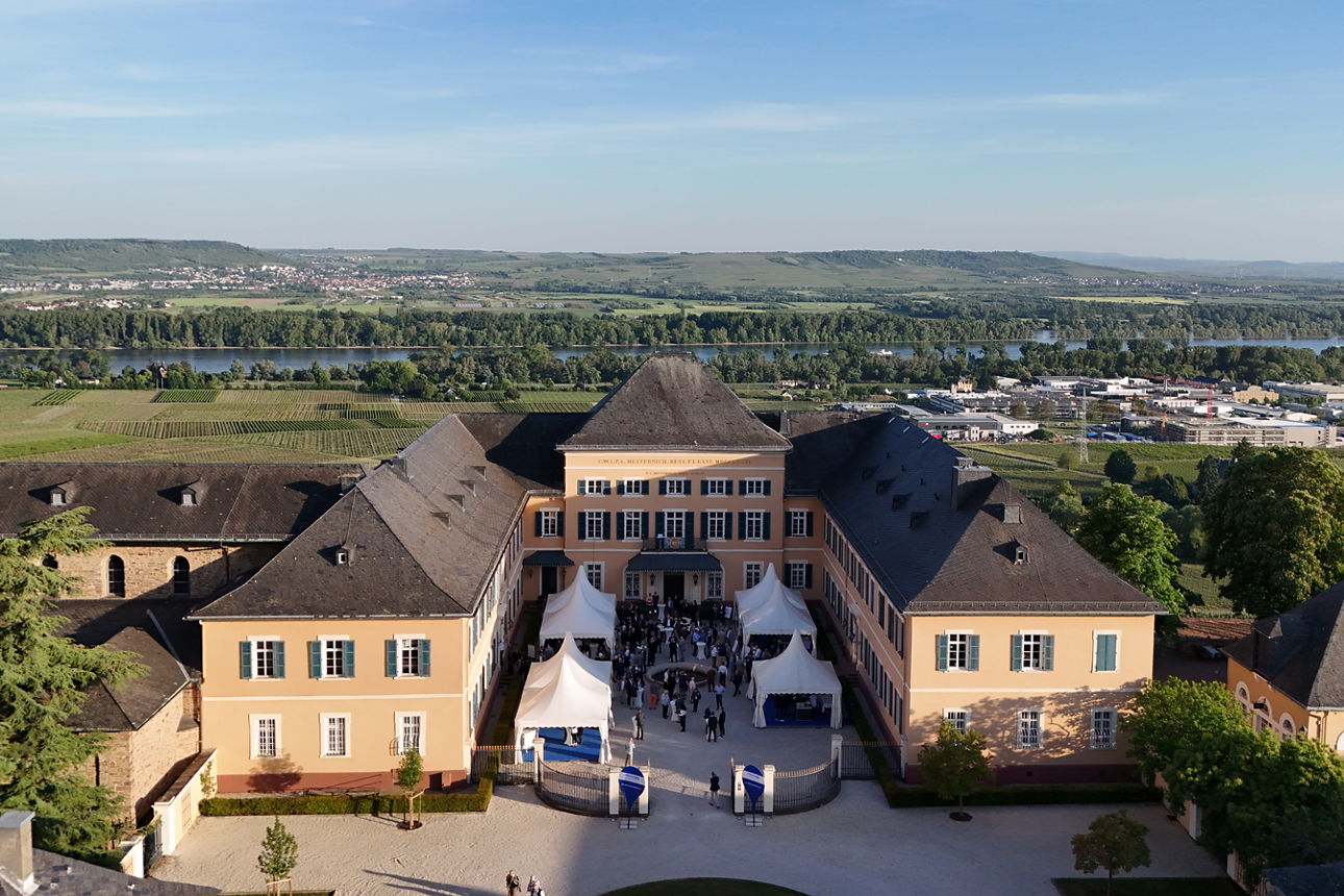 Luftaufnahme von Schloss Johannisberg im Rheingau - im Schlosshof stehen Menschen - im Hintergrund sieht man Weinberge und den Rhein