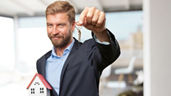 Mann hält einen Hausschlüsel und ein Haus in der Hand. 