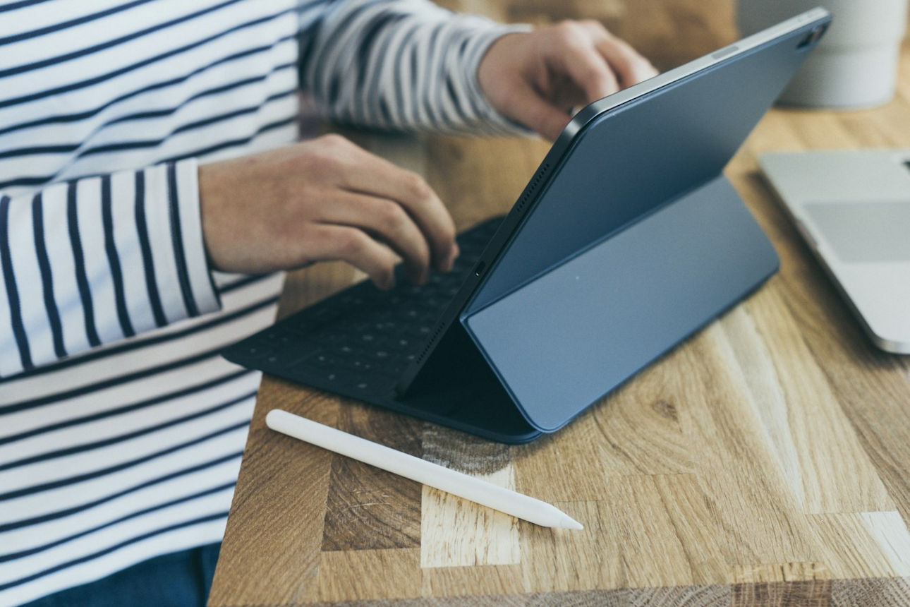 -Weibliche Person mit Streifenschirt am holzfarbenen Schreibtisch mit Tablet und Laptop sowie Grünpflanze im Hintergrund