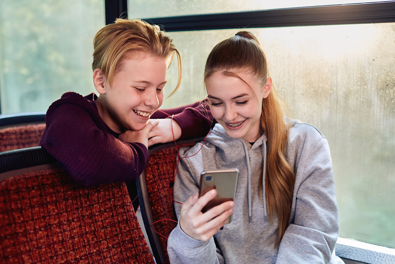 Ein Junge und ein Mädchen in einem Bus schauen gemeinsam in das Handy des Mädchens