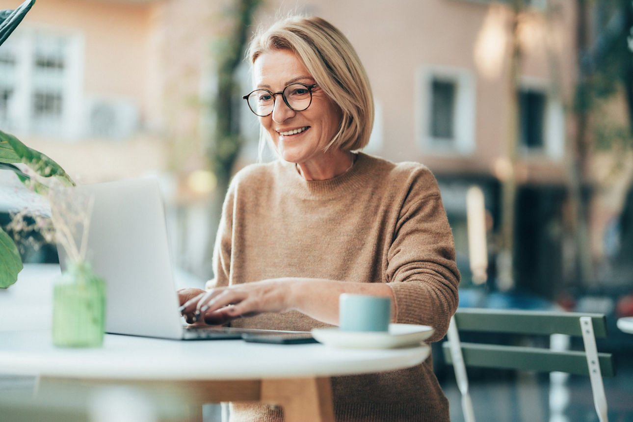 Frau sitzt in Café und arbeitet an ihrem Laptop