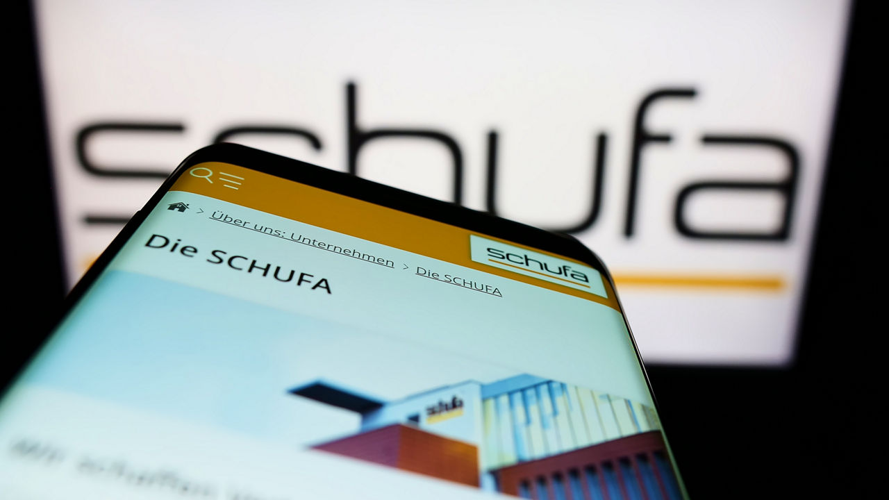 Mobiltelefon mit der Website der Schufa Holding AG vor dem Logo. Fokus oben links auf dem Display.