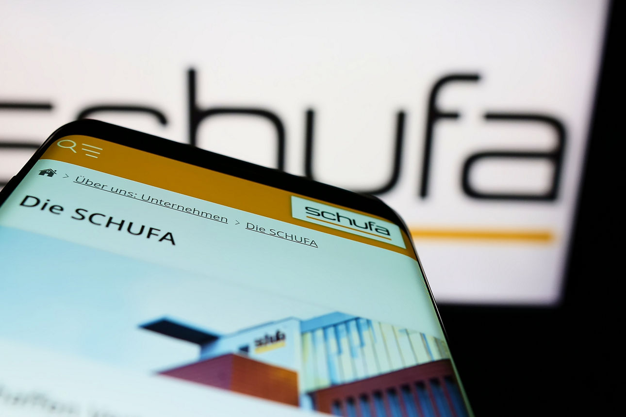 Mobiltelefon mit der Website der Schufa Holding AG vor dem Logo. Fokus oben links auf dem Display.