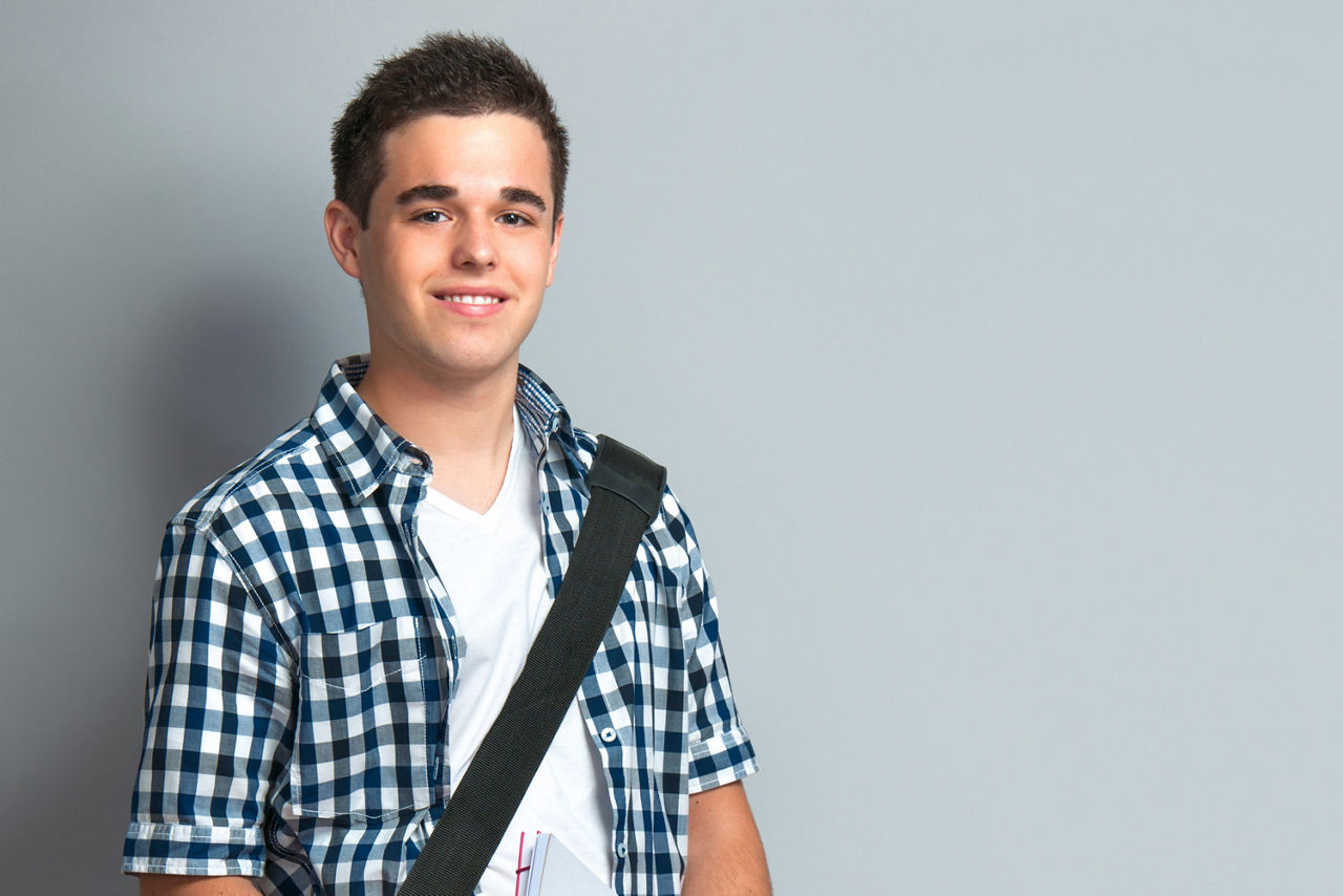 Schulservice - Junge mit kariertem Hemd und Schultasche lächelt in die Kamera