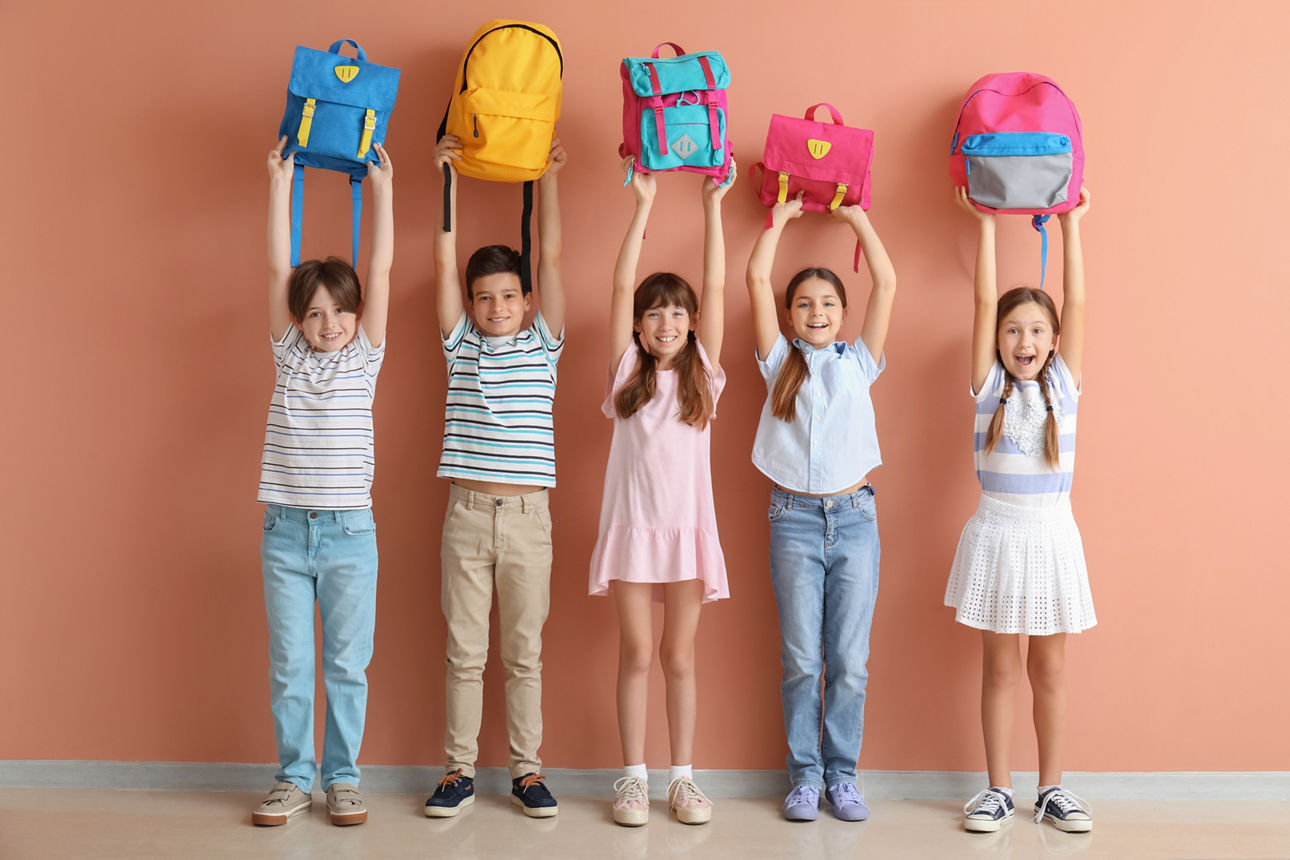 Fünf Kinder halten ihre Schulranzen in die Höhe