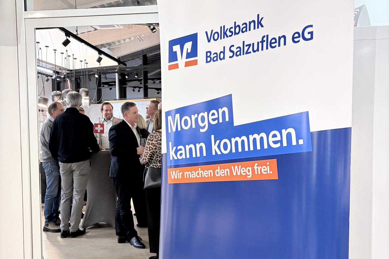 Neben einem Banner der Volksbank Bad Salzuflen unterhalten sich Kunden an Stehtischen