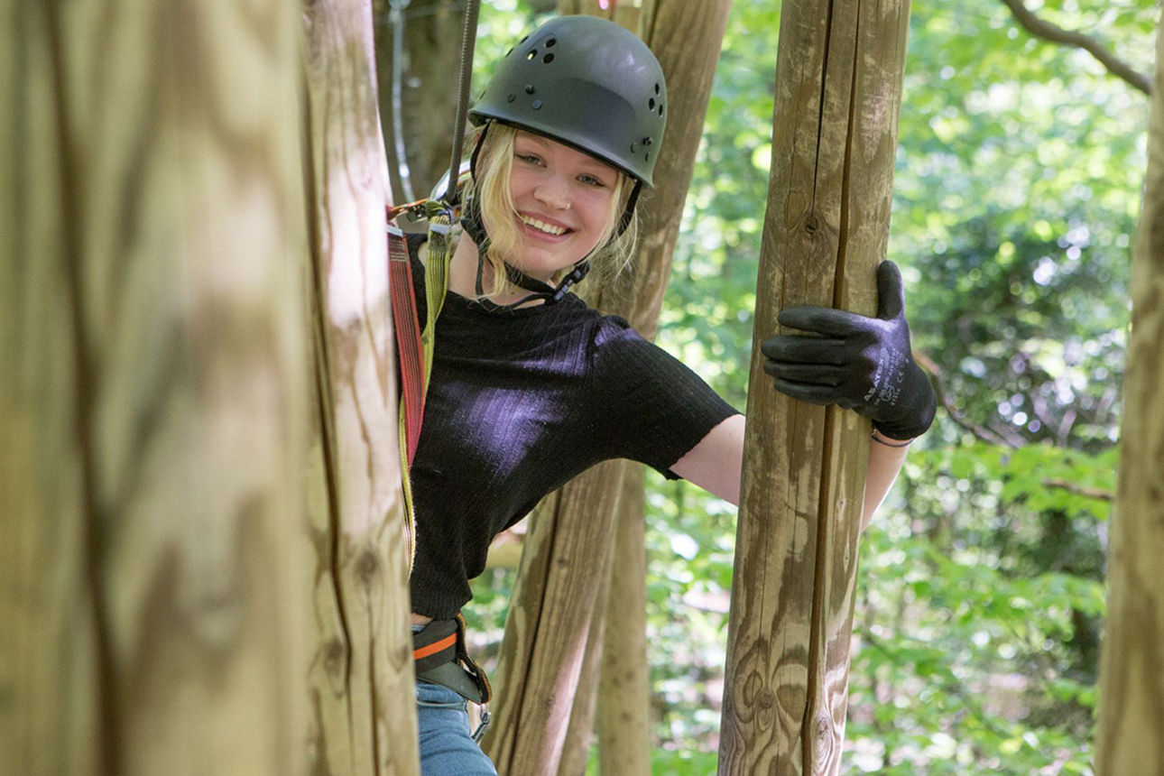 Eine Person schießt mit einem Bogen auf ein Spinnennetz. In der Ecke ist das Logo des Kletterparks Schwindelfrei.