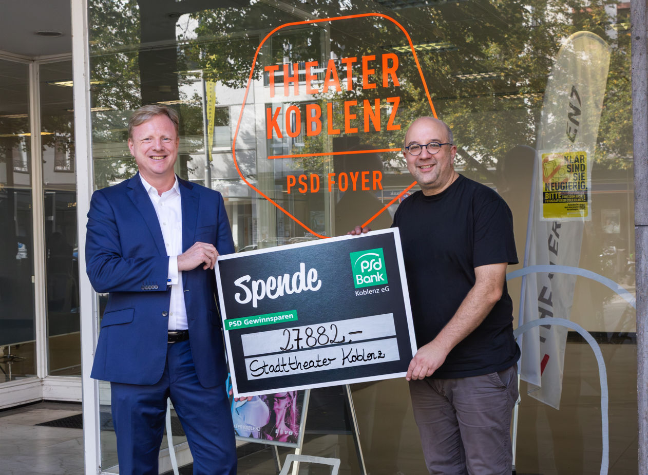 zwei Personen halten einen Spendenscheck und schauen dabei in die Kamera