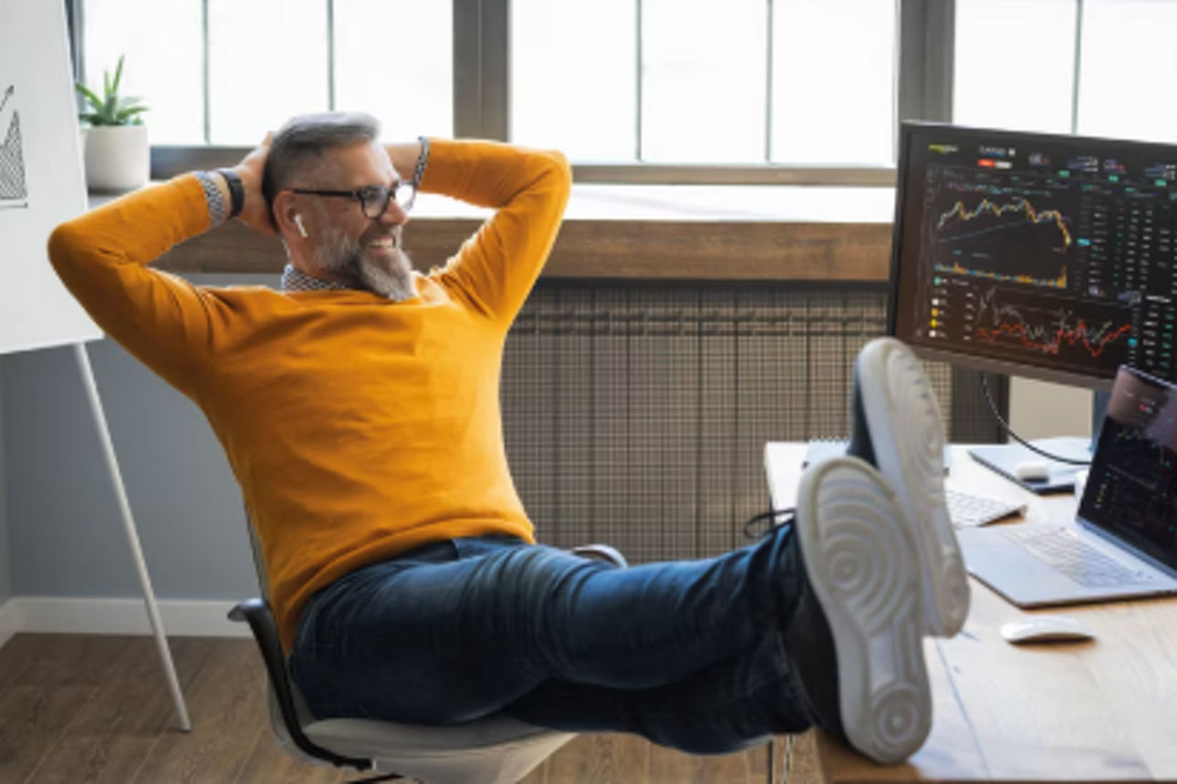 Mann sitzt am Schreibtisch und schaut sich die Börseninformationen am PC an