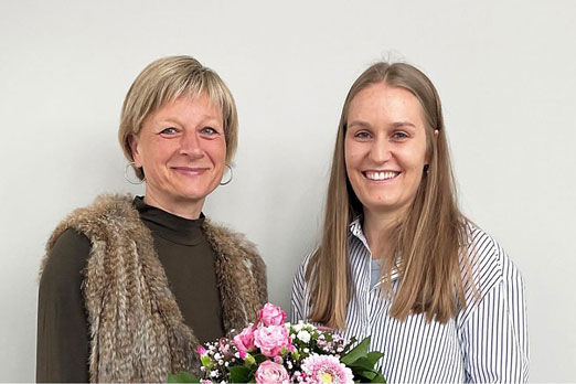 Zwei Frau lächelnd und eine hält einen Blumenstraß in der Hand