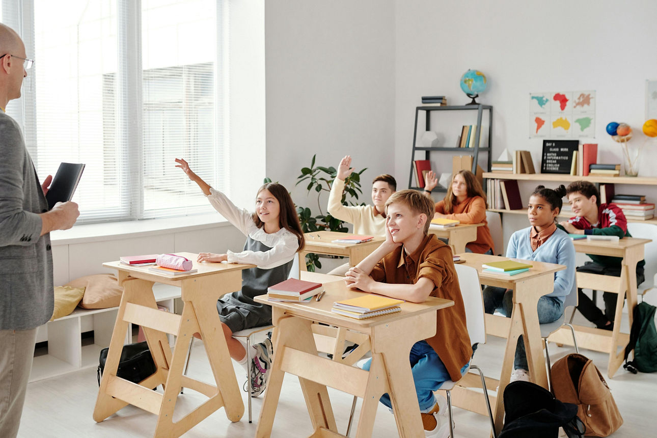 Sechs Schüler sitzen in einem Klassenraum und hören einem Lehrer zu
