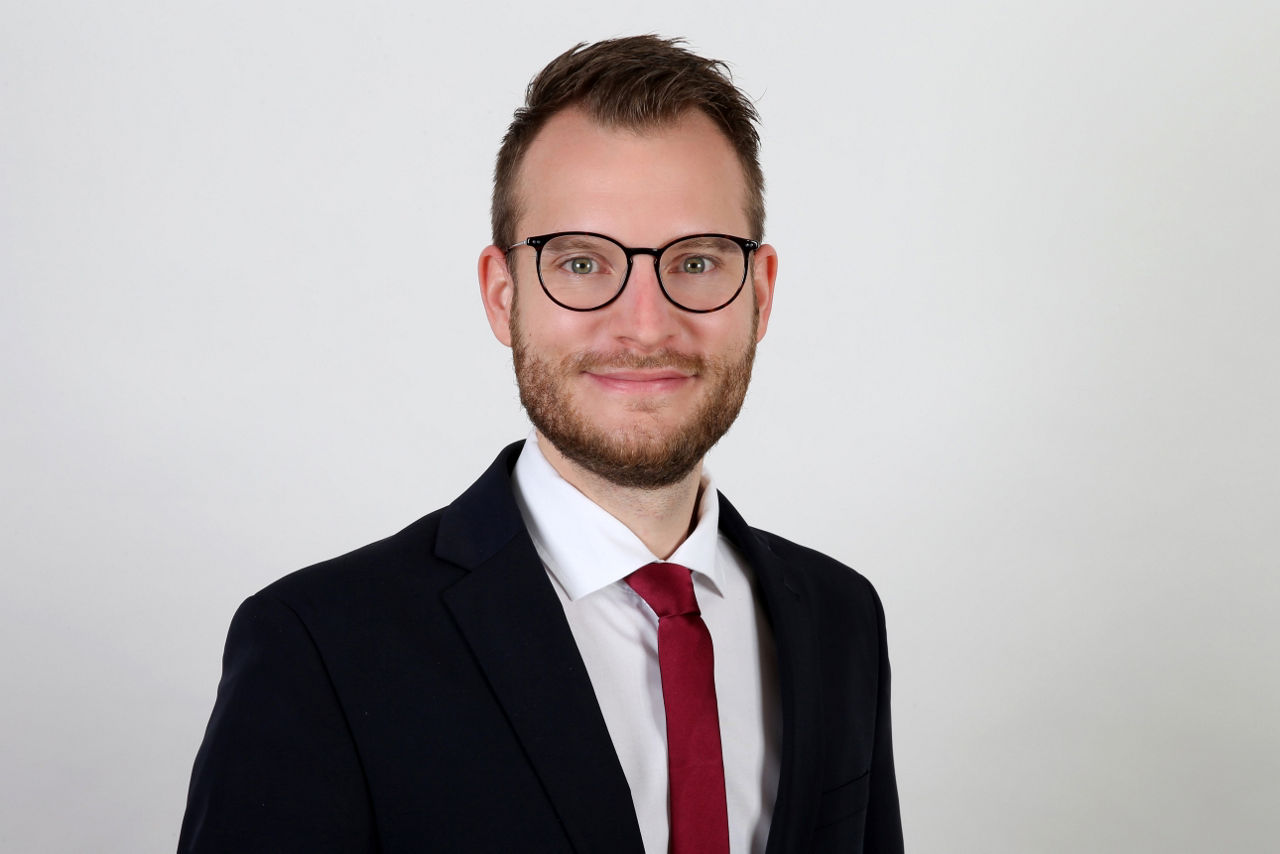 Ein lächelnder Mann in einem Anzug schaut in die Kamera.