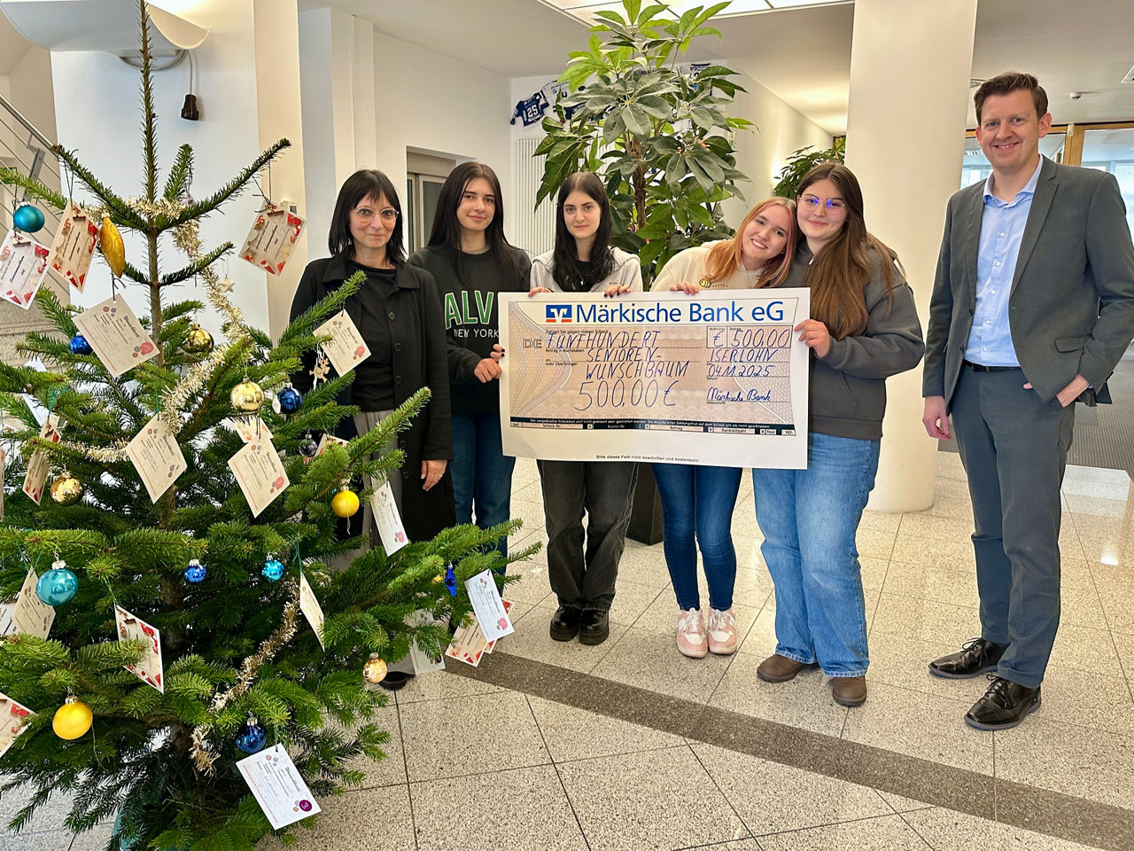 M. Cussel, Gabriele, Greta, Lillian-Lu und Sonila mit Filialleiter André Deimel mit dem Übergabescheck bei den Wunschbäumen.
