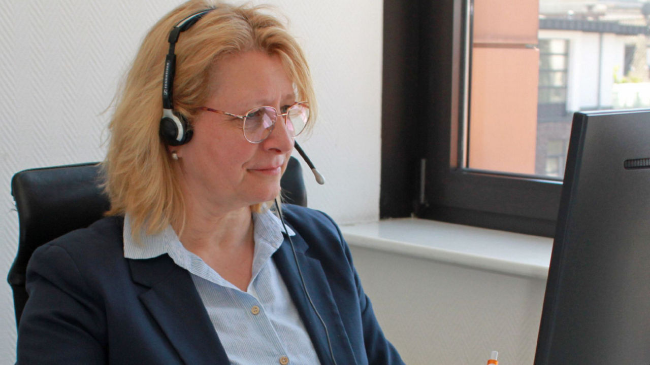 Eine Frau mit Headset sitzt lächelnd an ihrem Arbeitsplatz