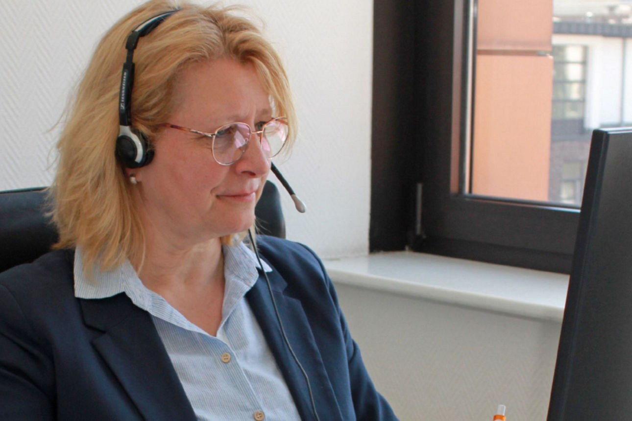 Eine Frau mit Headset sitzt lächelnd an ihrem Arbeitsplatz
