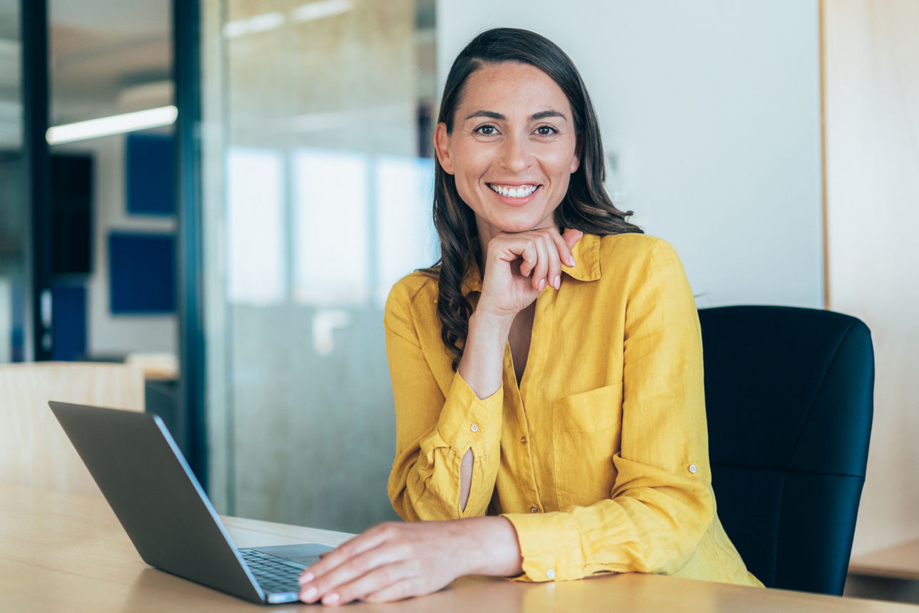 Junge Frau lächelt zufrieden vor einem Laptop im Büro
